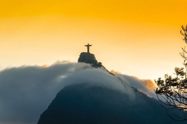 Vista panorâmica do Cristo Redentor no Rio de Janeiro, com a cidade e a Baía de Guanabara ao fundo, destacando o céu azul e a natureza ao redor